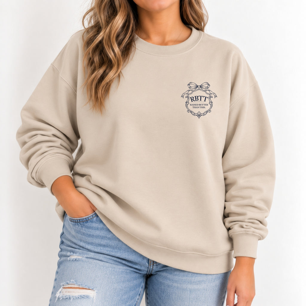 Woman wearing the Raised Better Than This crest crewneck sweatshirt in Sand with a navy left-chest crest