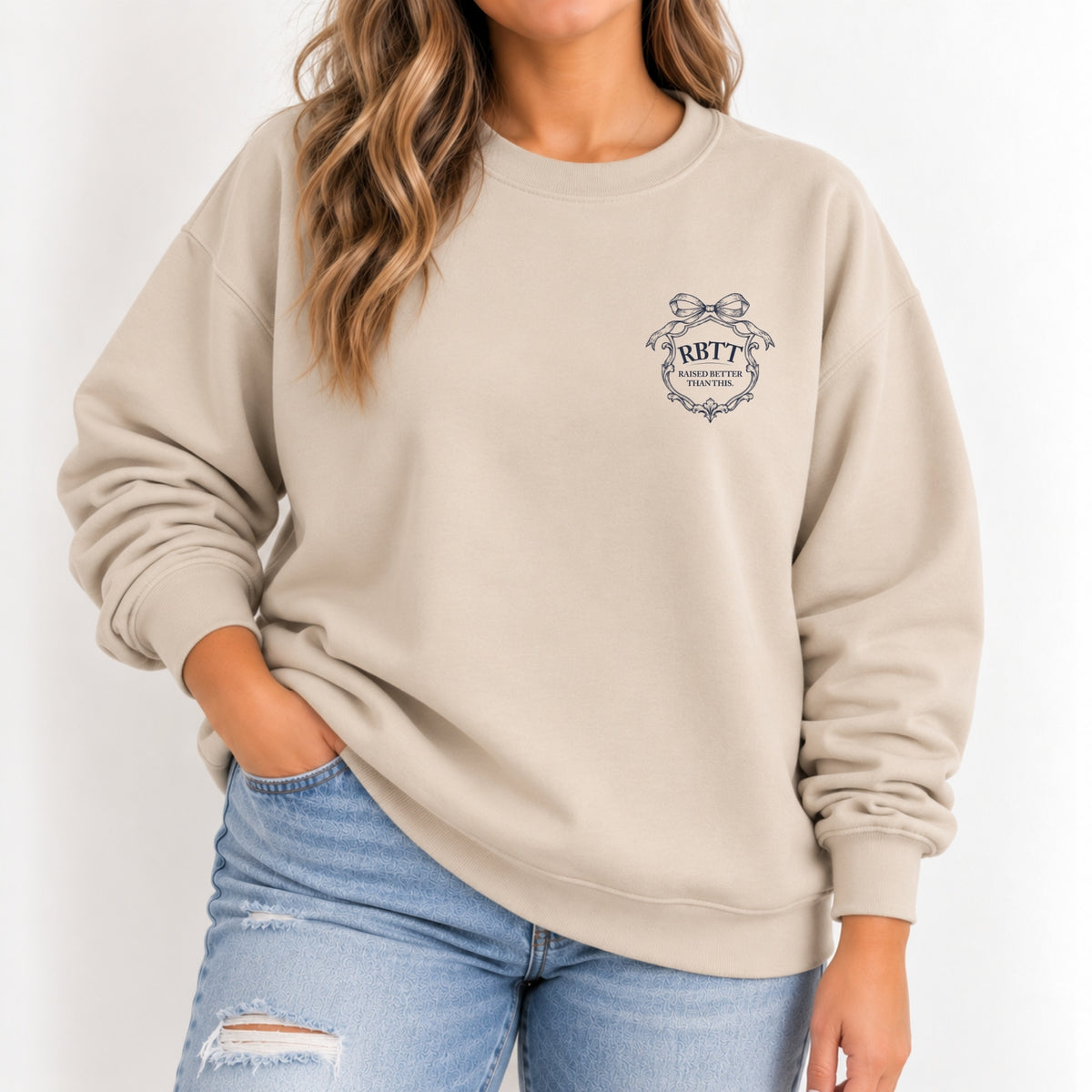 Woman wearing the Raised Better Than This crest crewneck sweatshirt in Sand with a navy left-chest crest