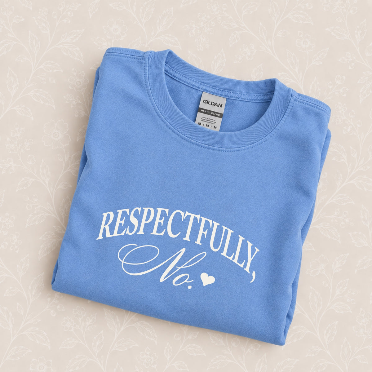 Respectfully, No crewneck in Carolina Blue folded on a cream floral surface, chest design close up
