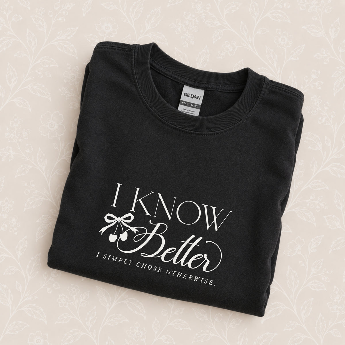 I Know Better, I Simply Chose Otherwise crewneck in Black folded on a cream floral surface, chest design close up