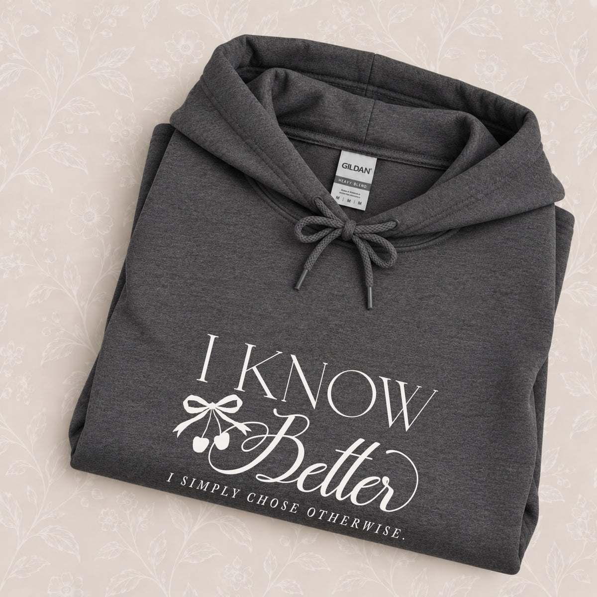 I Know Better, I Simply Chose Otherwise hoodie in Dark Heather folded on a cream floral surface, chest design close up