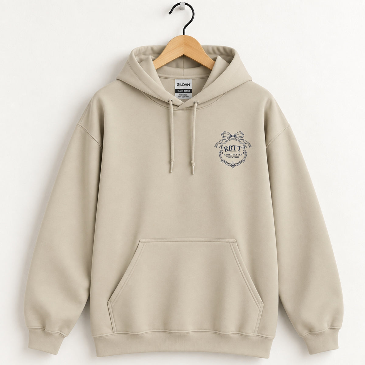 Raised Better Than This crest hoodie in Sand on a wooden hanger, navy left-chest crest