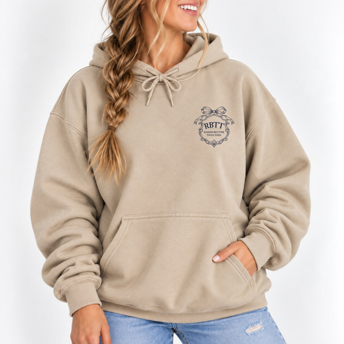 Woman wearing the Raised Better Than This crest hoodie in Sand with a navy left-chest crest