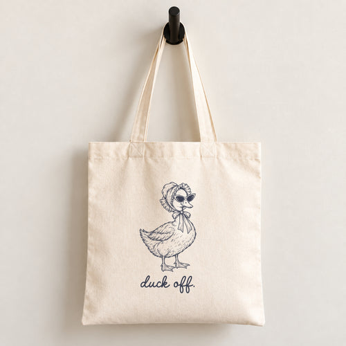 Duck Off natural canvas tote bag hanging on a wall hook, navy duck in a bonnet and sunglasses printed on the front