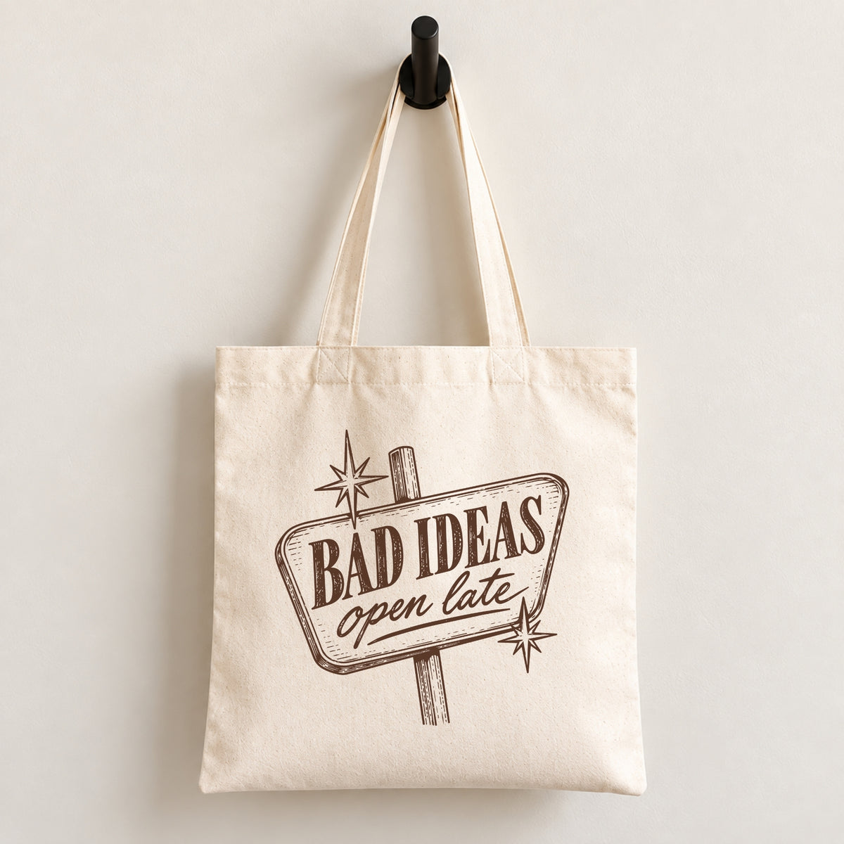 Bad Ideas, Open Late canvas tote bag hanging on a wall hook, retro sign printed in brown