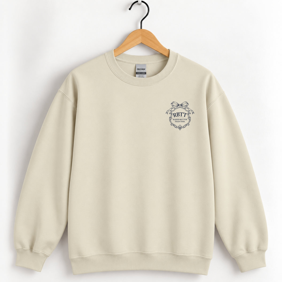 Raised Better Than This crest crewneck sweatshirt in Sand on a wooden hanger, navy left-chest crest