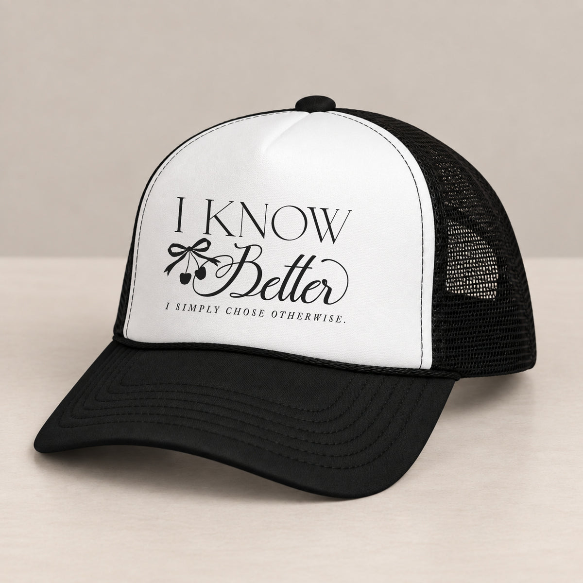 I Know Better trucker hat in Black on a table, angled view showing the mesh back and curved bill