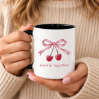 Mostly Together cherry bow mug with black handle and interior, held in both hands