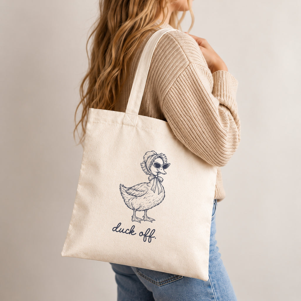 Woman in a tan sweater carrying the Duck Off canvas tote on her shoulder