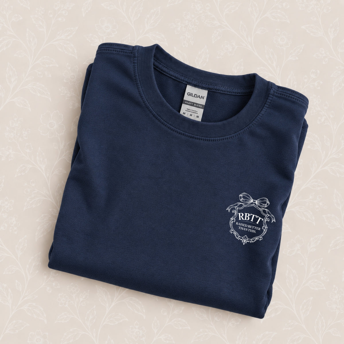 Raised Better Than This crest crewneck sweatshirt in Navy folded on a cream floral surface, crest close up