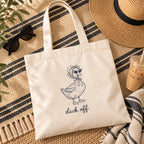 Duck Off canvas tote flat lay with a straw hat, sunglasses and an iced coffee on a striped blanket