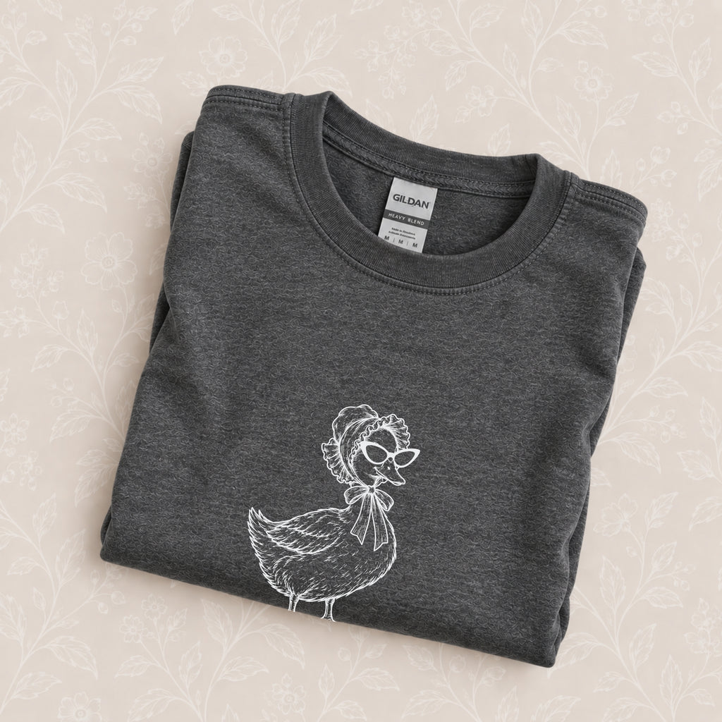 Duck Off crewneck in Dark Heather folded on a cream floral surface, close up of the white duck in a bonnet