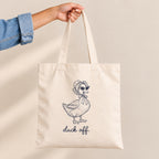 Hand holding the Duck Off natural canvas tote by its long handles, duck design close up