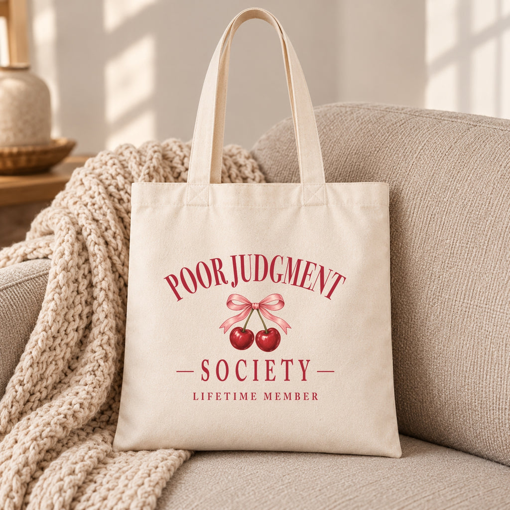 Poor Judgment Society Lifetime Member canvas tote bag resting on a sofa with a knit throw
