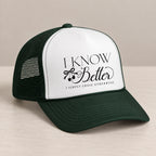 I Know Better trucker hat in Dark Green on a table, angled view showing the mesh back and curved bill