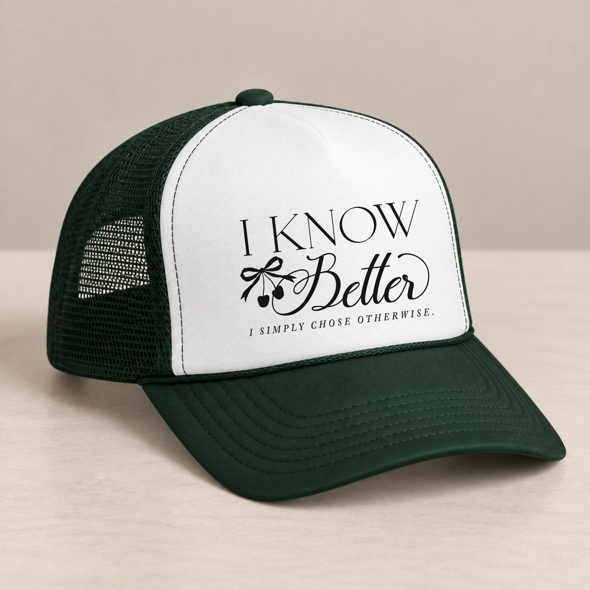 I Know Better trucker hat in Dark Green on a table, angled view showing the mesh back and curved bill