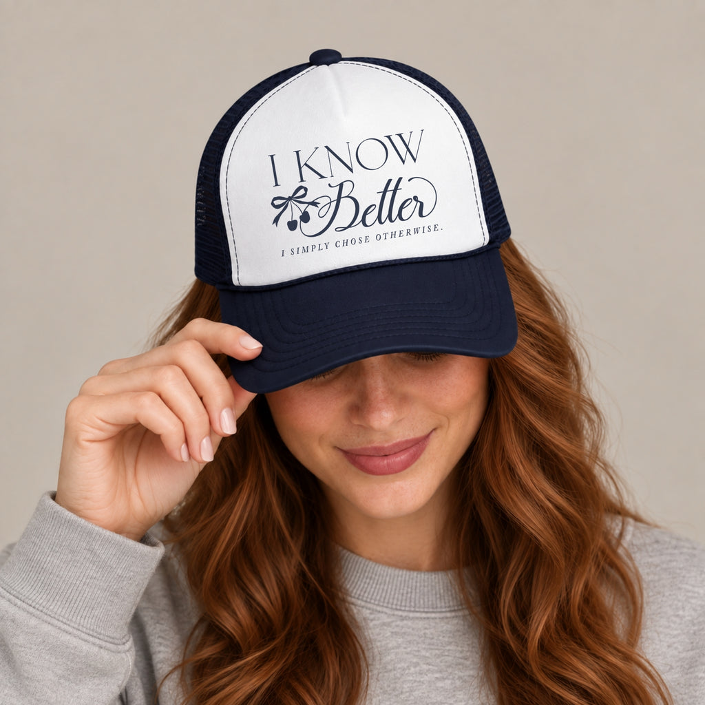 Woman in a grey sweatshirt tipping the brim of the I Know Better trucker hat in Navy