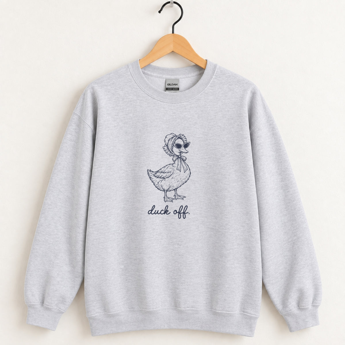 Duck Off crewneck sweatshirt in Ash on a wooden hanger, navy duck design center chest