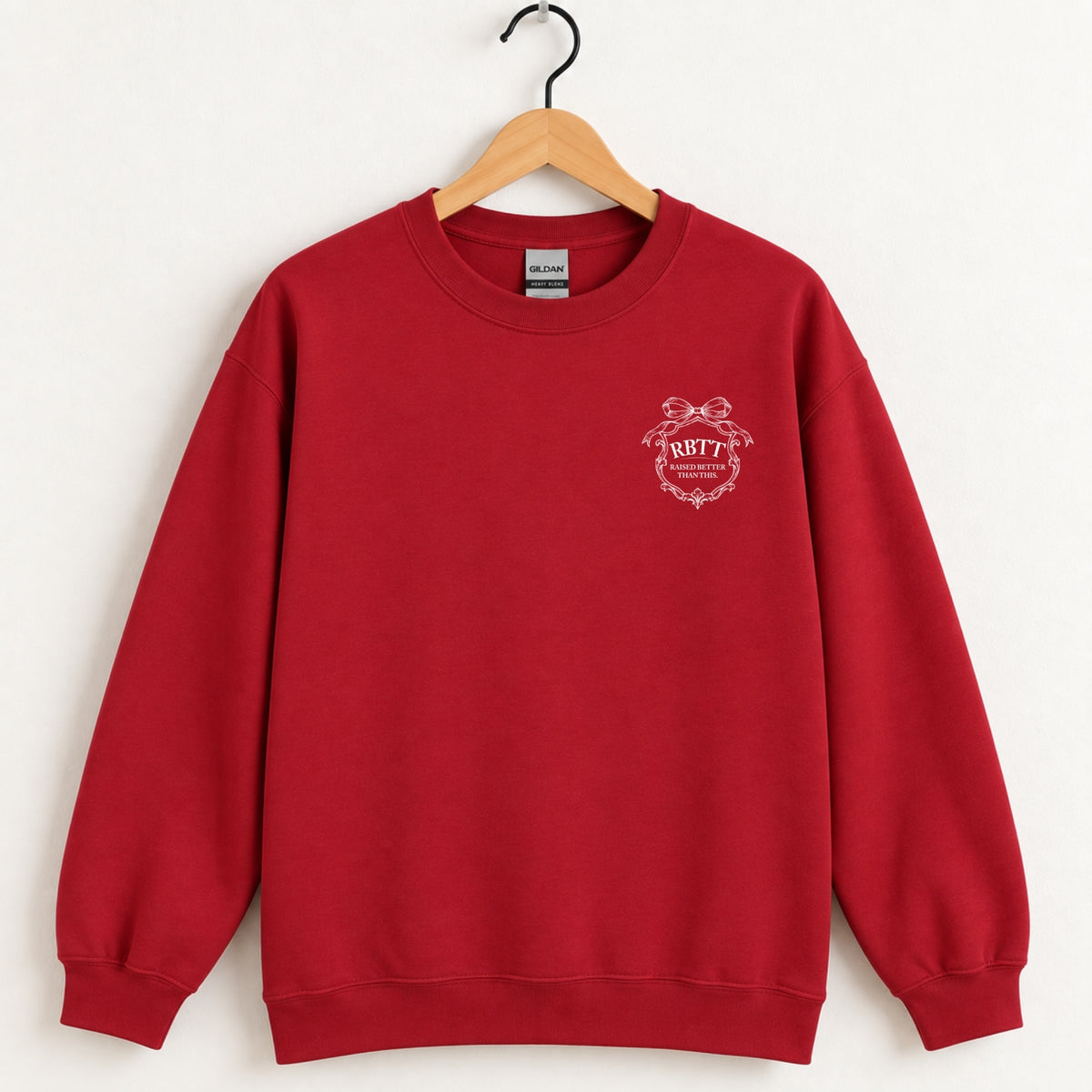 Raised Better Than This crest crewneck sweatshirt in Cardinal Red on a wooden hanger