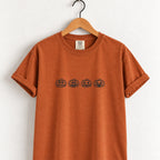 Jack-o-lantern embroidered tee in Yam on a wooden hanger, four black-thread pumpkins across the chest