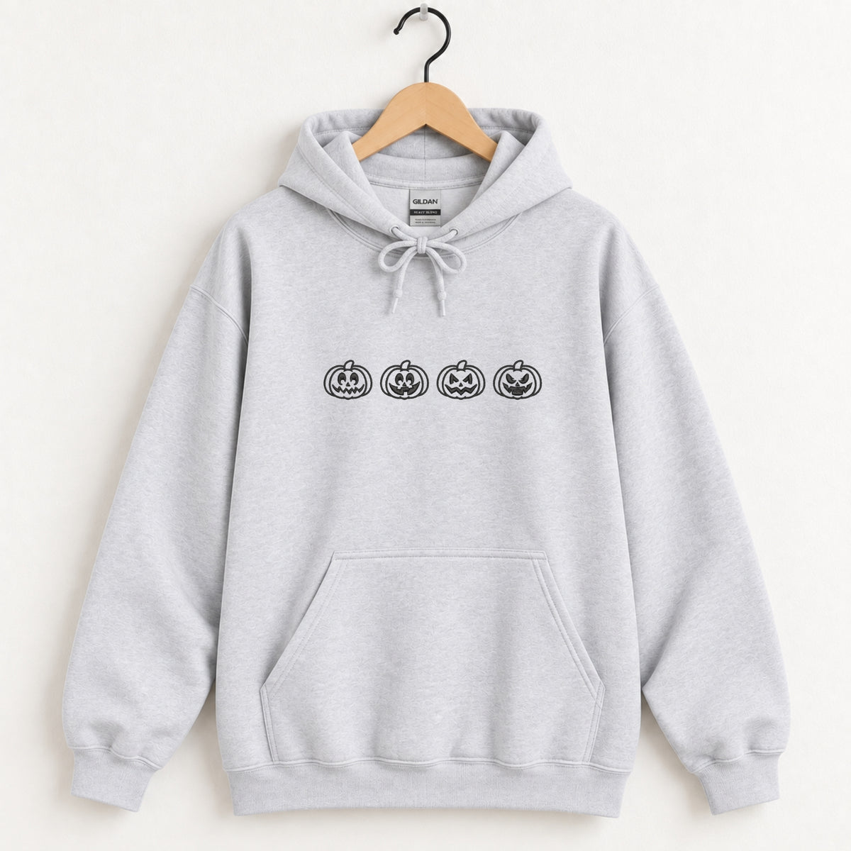 Jack-o-lantern embroidered hoodie in Ash on a wooden hanger, black thread pumpkins