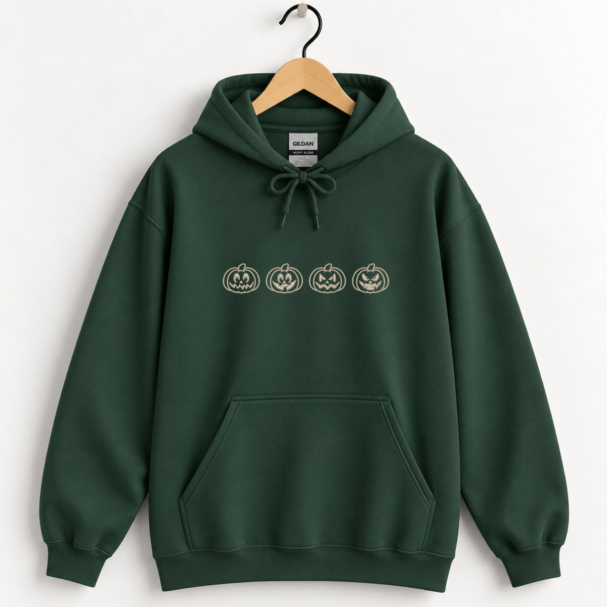Jack-o-lantern embroidered hoodie in Forest Green on a wooden hanger, ivory thread pumpkins