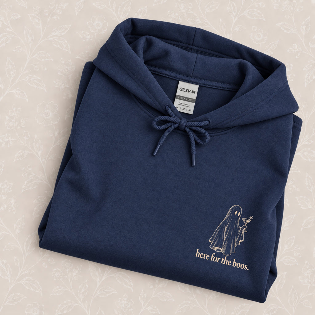 Here for the Boos hoodie in Navy folded on a cream floral surface, close up of the ivory ghost and martini print