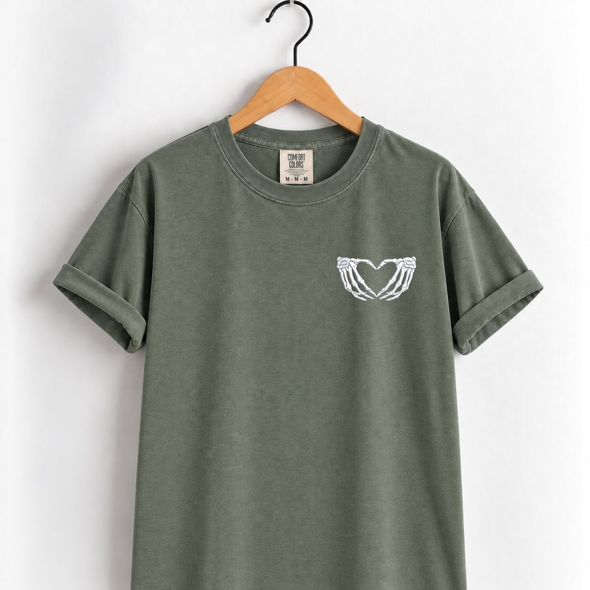 Heart hands skeleton embroidered tee in Moss on a wooden hanger