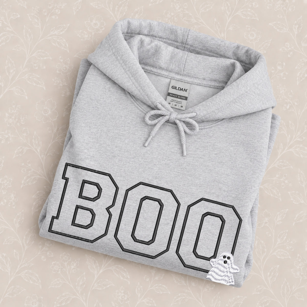 Boo embroidered hoodie in Ash folded on a cream floral surface, close up of the varsity BOO and ghost embroidery