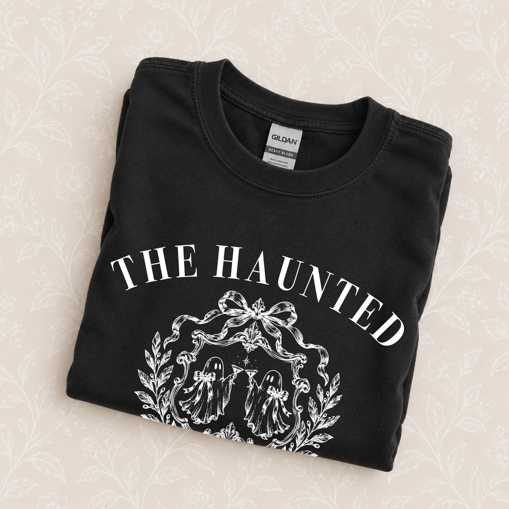 The Haunted Social Club crewneck sweatshirt in Black folded on a cream floral surface, close up of the ghost crest