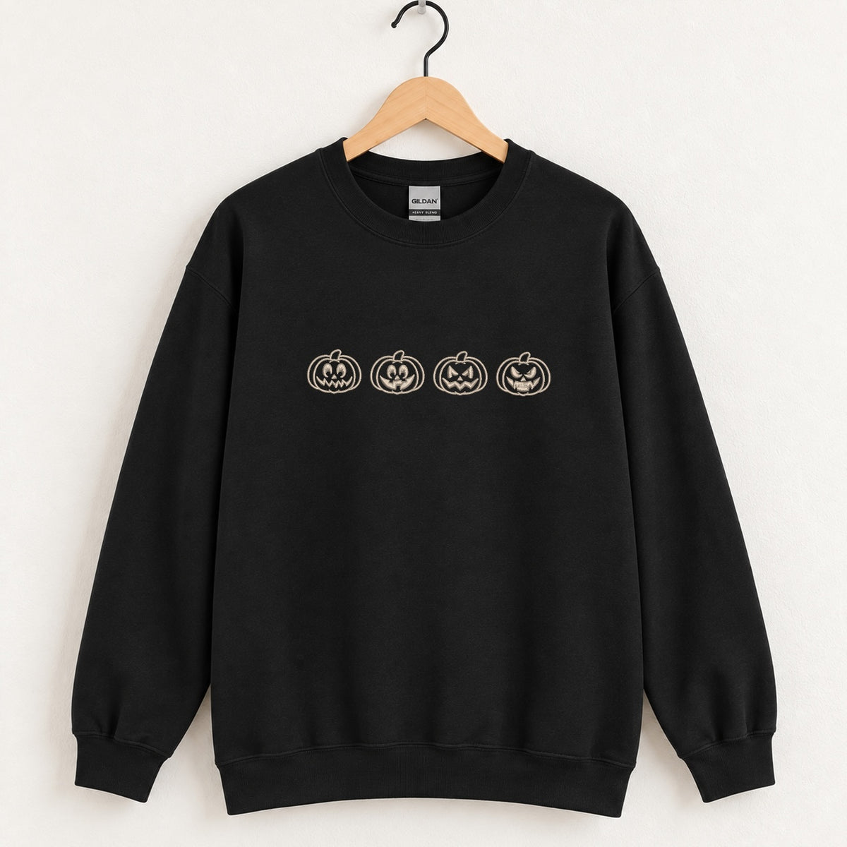 Jack-o-lantern embroidered crewneck sweatshirt in Black on a wooden hanger, four ivory pumpkins across the chest