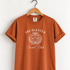 The Haunted Social Club tee in Yam (burnt orange) on a wooden hanger