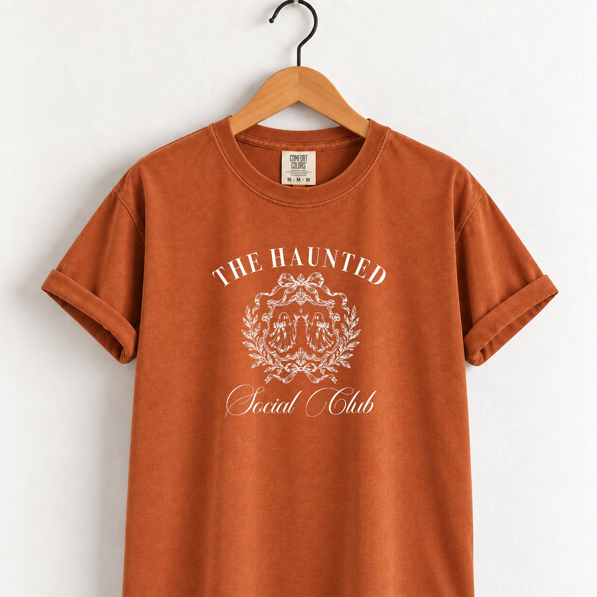 The Haunted Social Club tee in Yam (burnt orange) on a wooden hanger