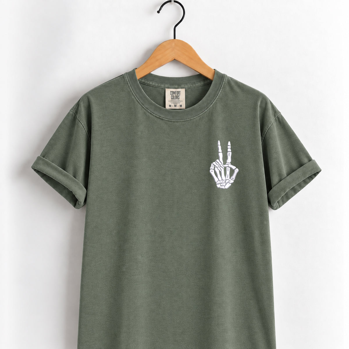 Peace sign skeleton hand embroidered tee in Moss on a wooden hanger, white thread left chest