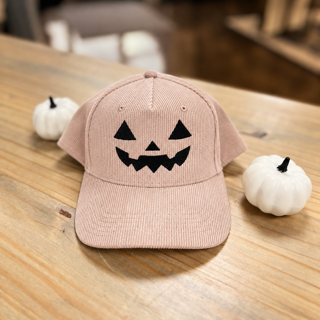 Jack-o-lantern embroidered corduroy snapback hat in Dusty Rose with a black thread pumpkin face, on a wooden table