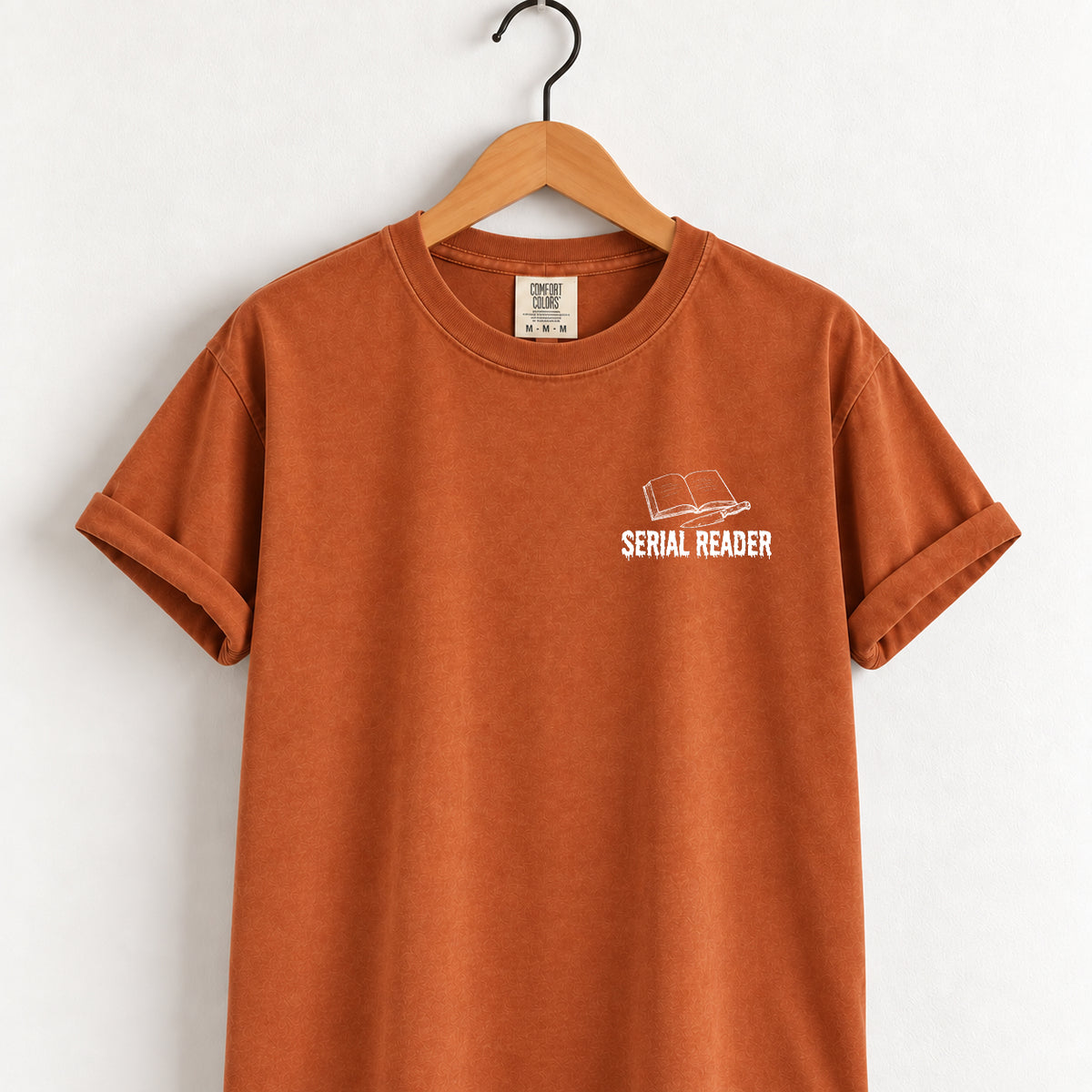 Serial Reader tee in Yam (burnt orange) on a wooden hanger