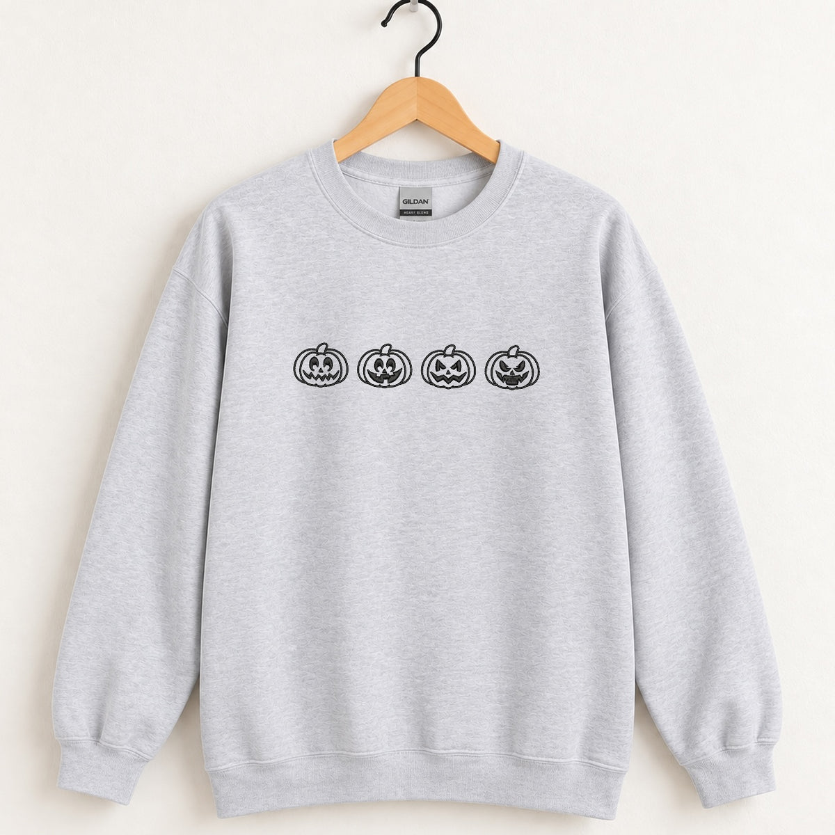 Jack-o-lantern embroidered crewneck sweatshirt in Ash on a wooden hanger, black thread pumpkins