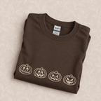 Jack-o-lantern embroidered crewneck sweatshirt folded on a cream floral surface, close up of the pumpkin embroidery