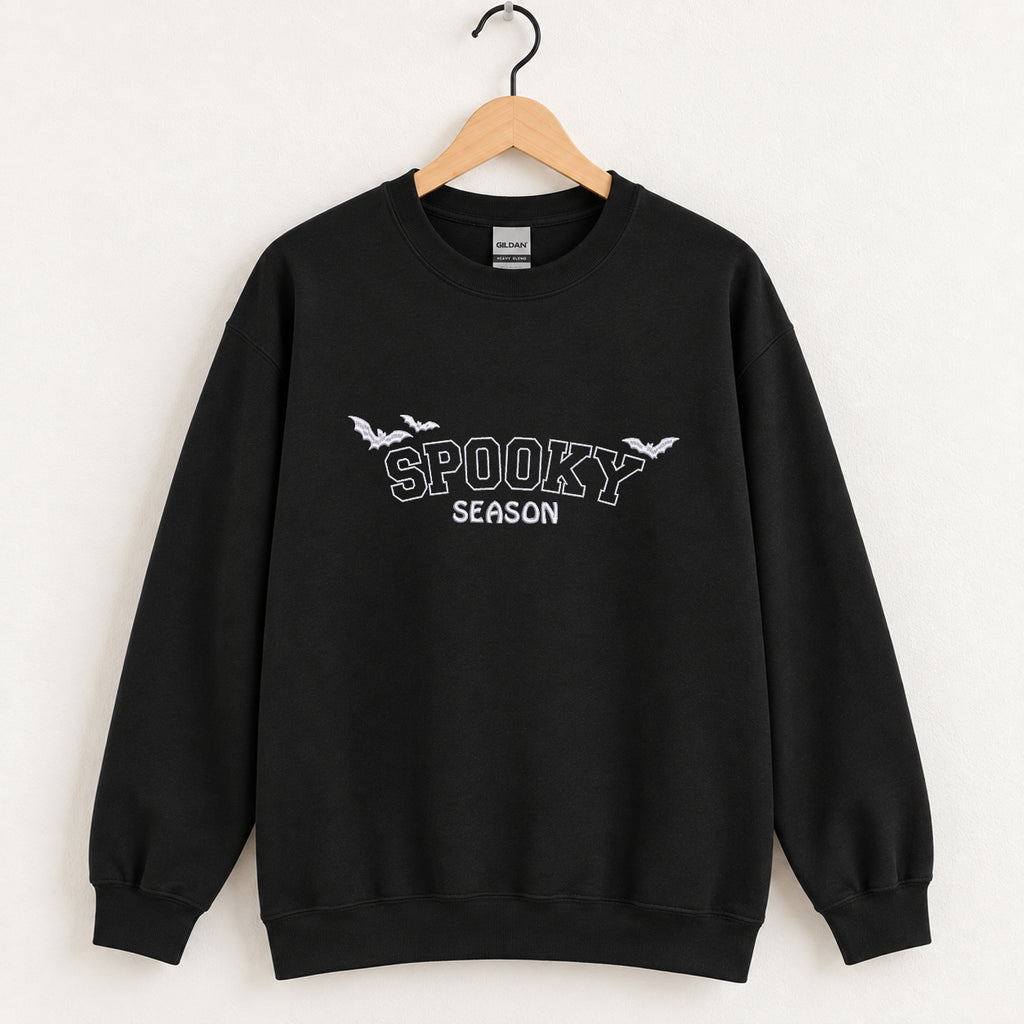 Spooky Season embroidered crewneck sweatshirt in Black on a wooden hanger, white thread lettering and bats