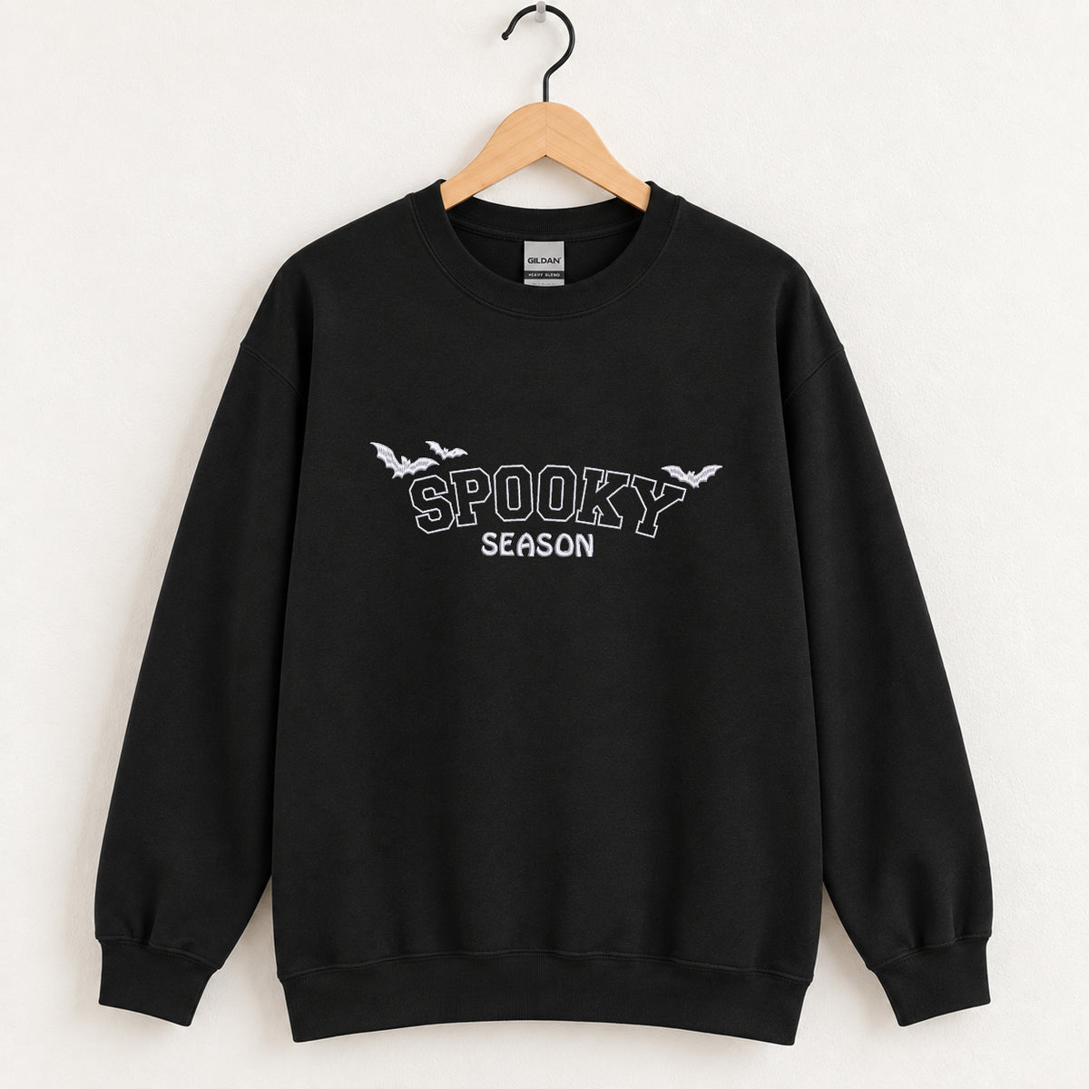 Spooky Season embroidered crewneck sweatshirt in Black on a wooden hanger, white thread lettering and bats