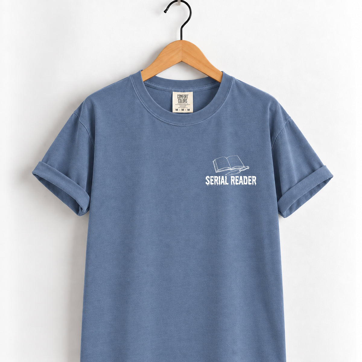 Serial Reader tee in Blue Jean on a wooden hanger, small white open-book left chest print
