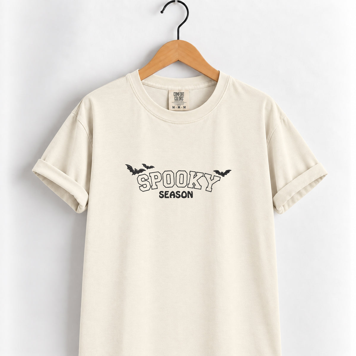Spooky Season embroidered tee in Ivory on a wooden hanger, black thread lettering with bats