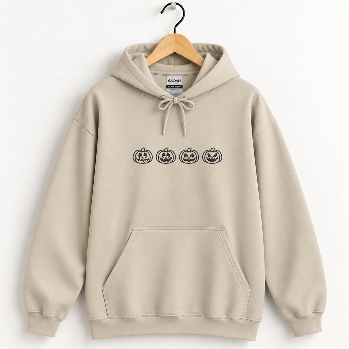 Jack-o-lantern embroidered hoodie in Sand on a wooden hanger, black thread pumpkins