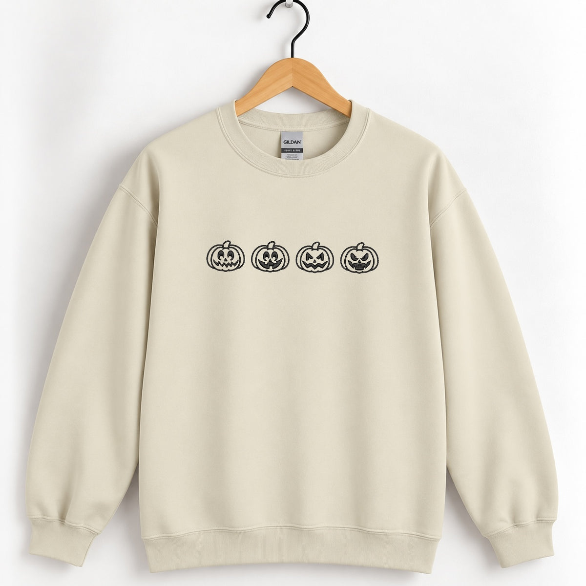 Jack-o-lantern embroidered crewneck sweatshirt in Sand on a wooden hanger, black thread pumpkins