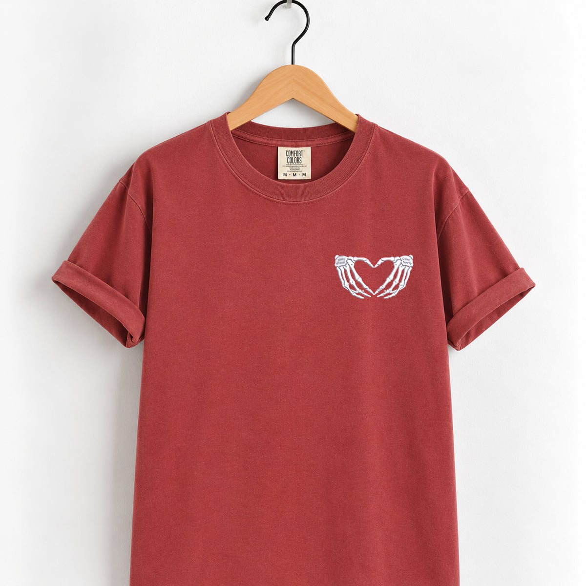 Heart hands skeleton embroidered tee in Chili on a wooden hanger, white thread left chest