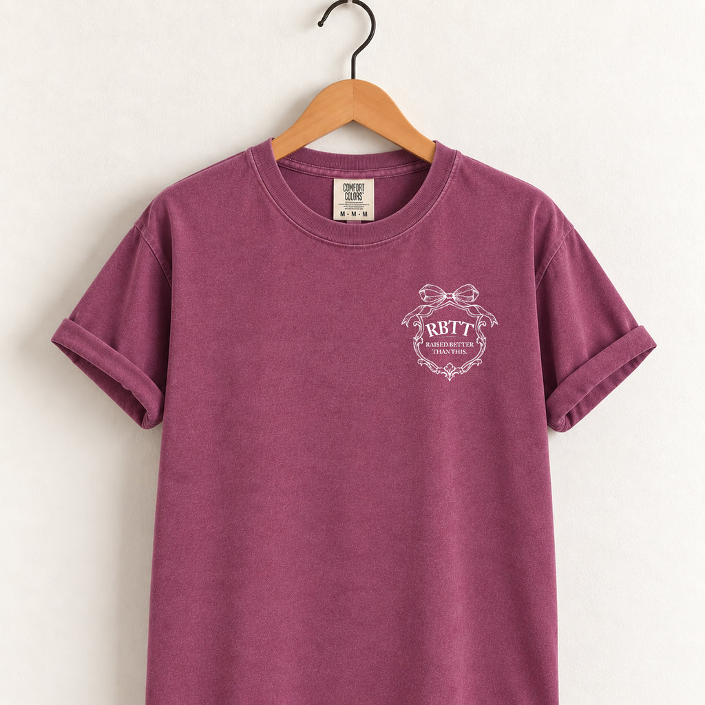 Raised Better Than This crest tee in Berry on a wooden hanger, left-chest RBTT logo with bow