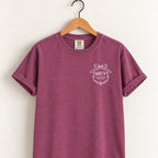 Raised Better Than This crest tee in Berry on a wooden hanger, left-chest RBTT logo with bow