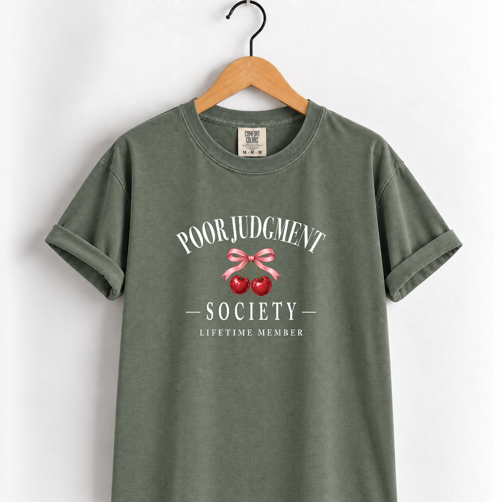 Poor Judgment Society Lifetime Member tee in Moss on a wooden hanger, cherry bow crest