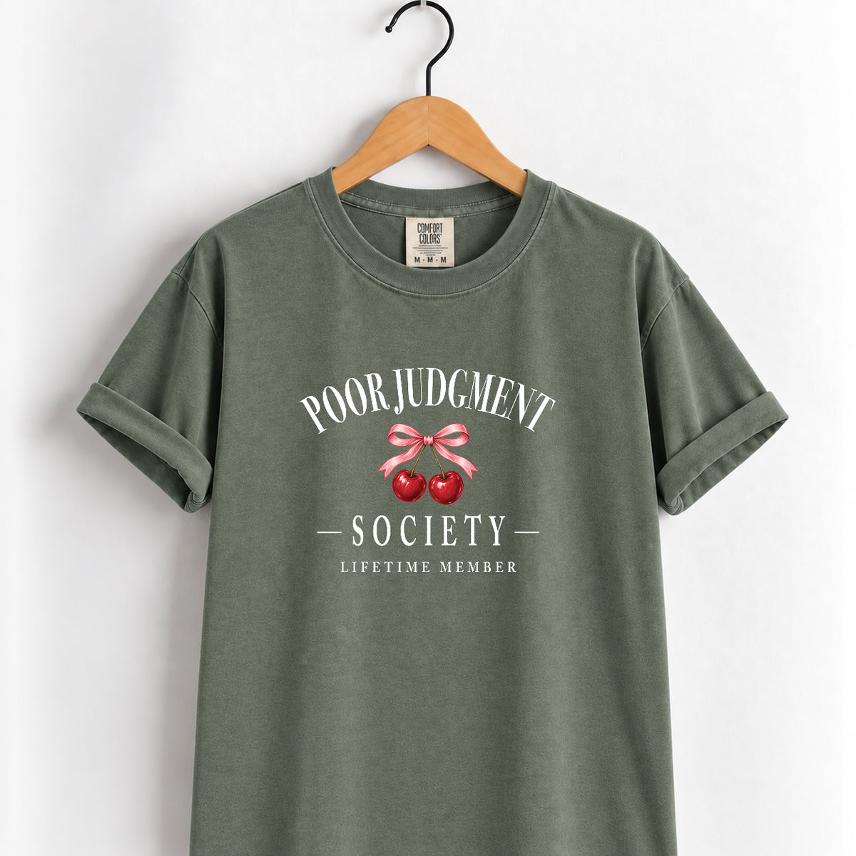 Poor Judgment Society Lifetime Member tee in Moss on a wooden hanger, cherry bow crest