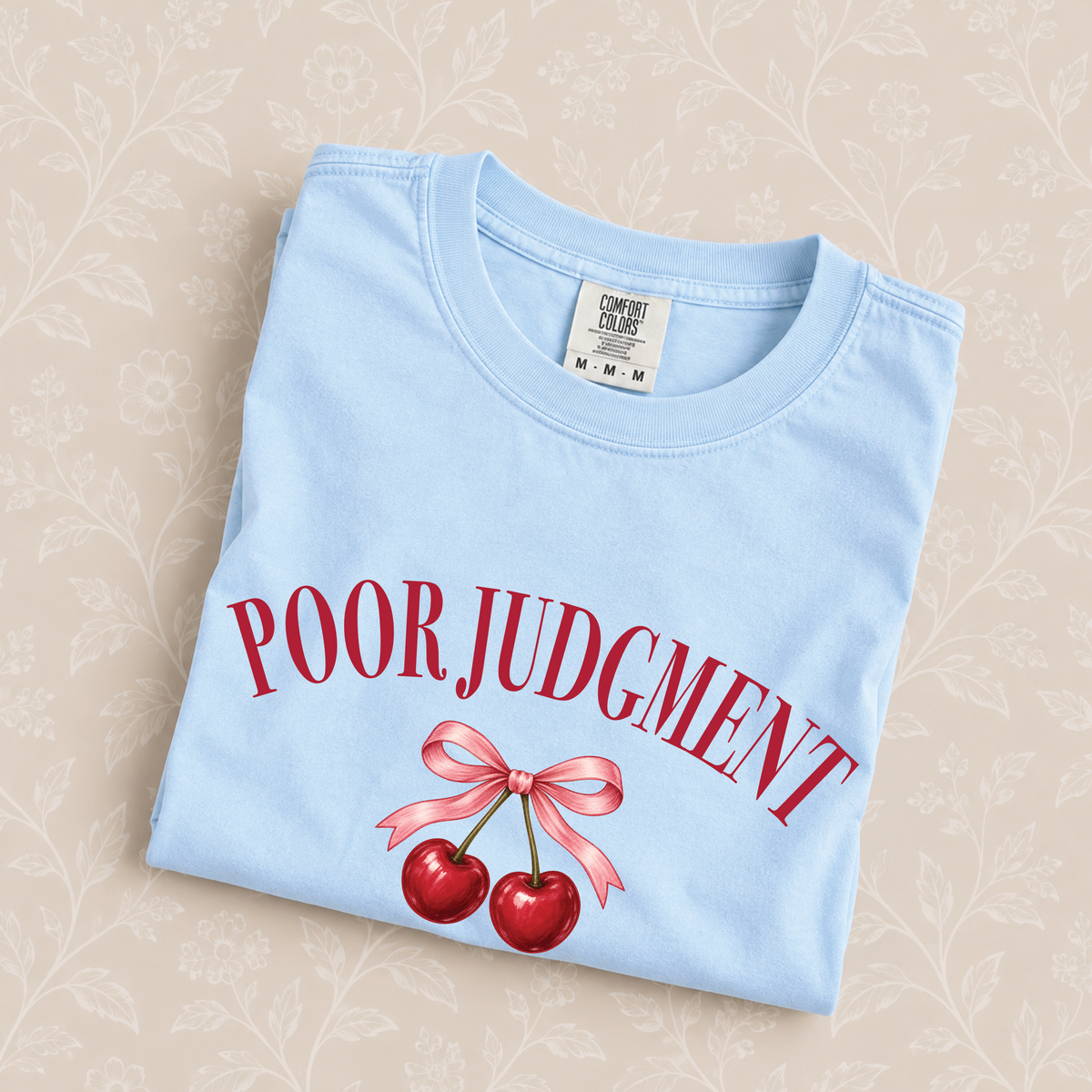 Poor Judgment Society Lifetime Member tee in Chambray folded on a cream floral surface, crest close up